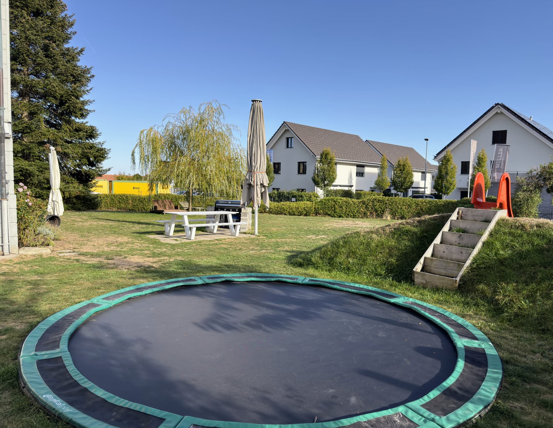 Im Boden eingelassenes Trampolin, Rutschbahn, Gasgrill und Sitzgarnitur im Garten