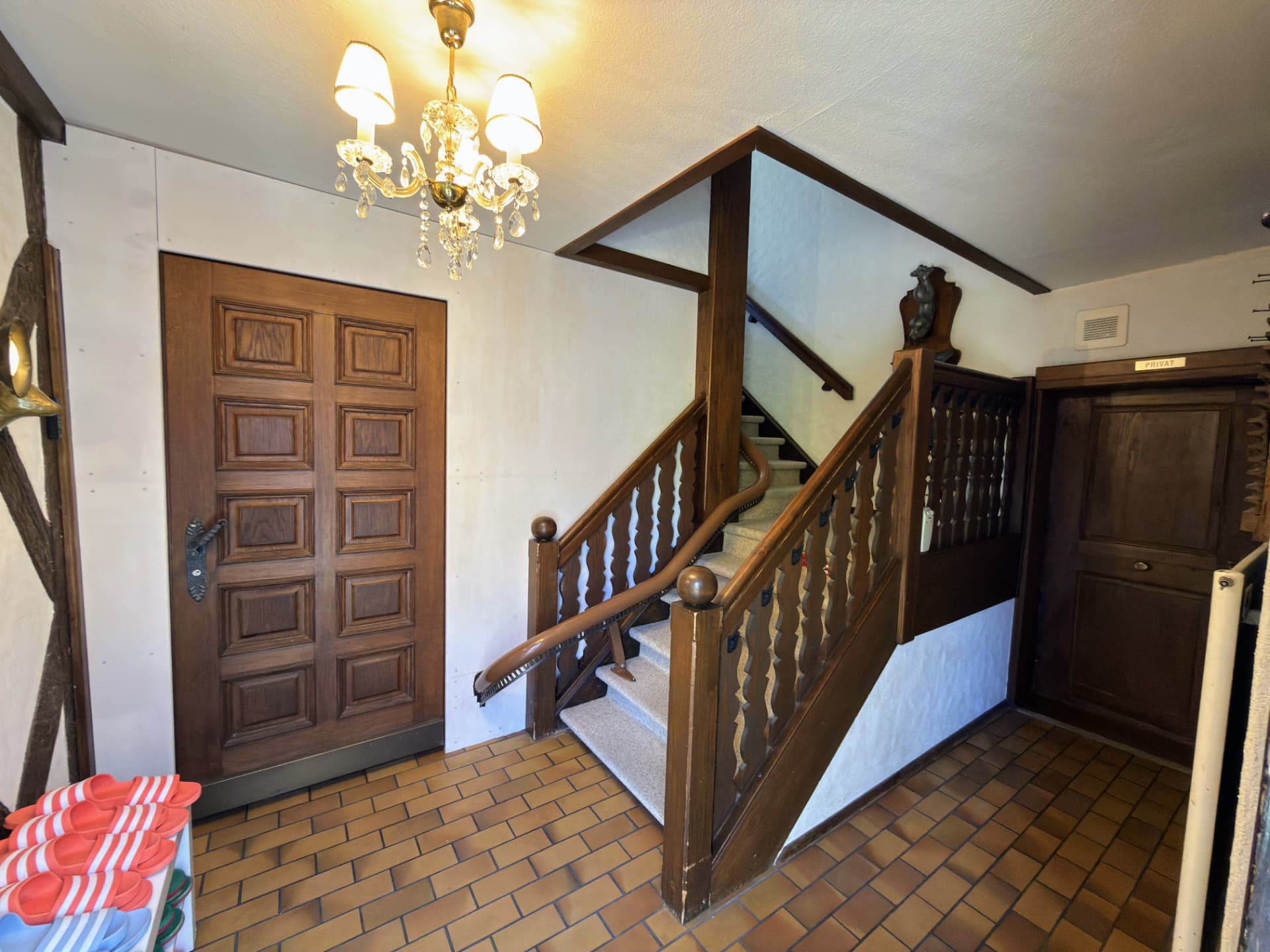 Eingangsbereich mit Kronleuchter, Holztreppe und Hausschuhen für die Gäste